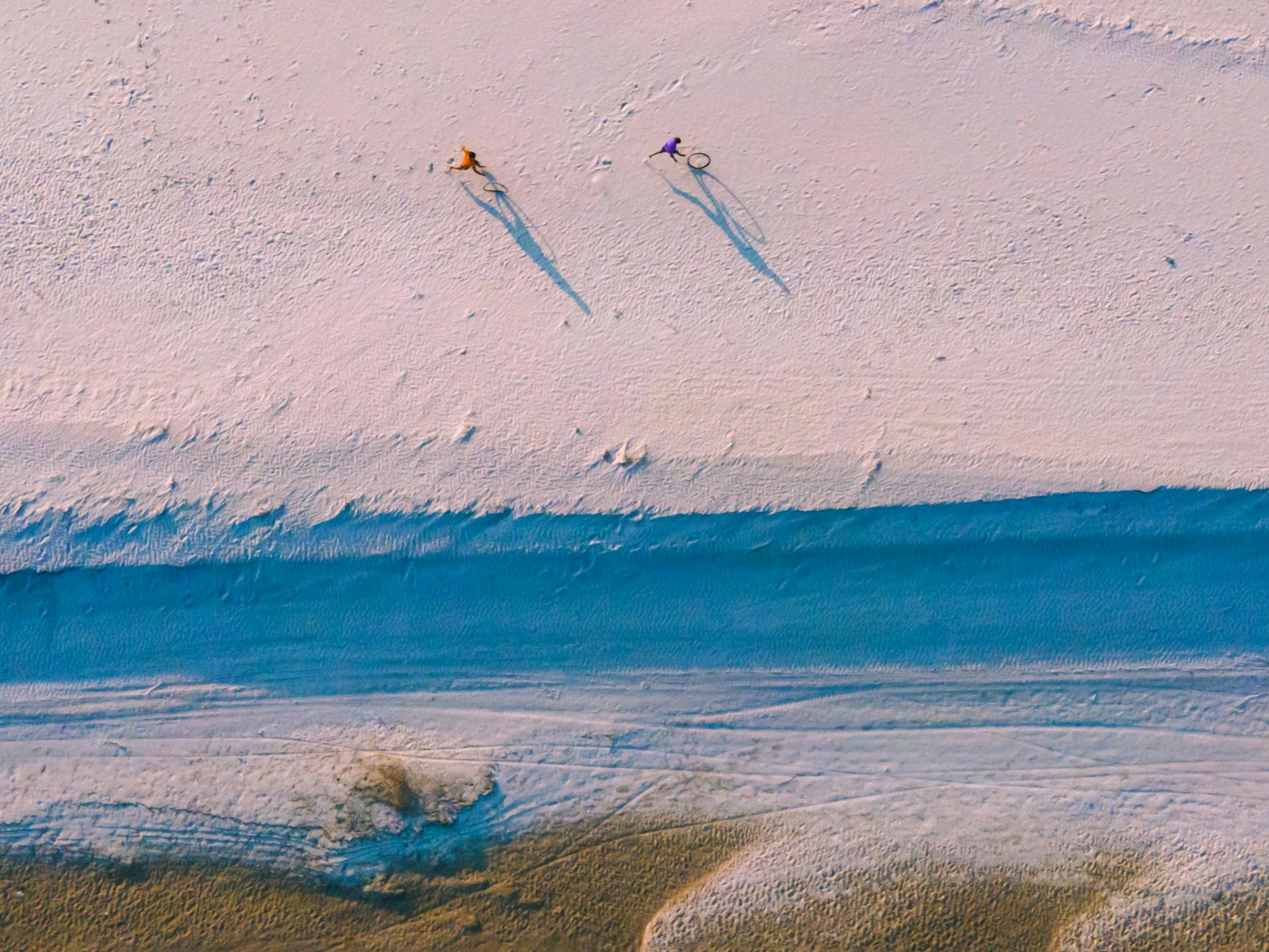 Dwóch rowerzystów jadących po piaszczystej plaży z lotu ptaka Dwóch rowerzystów jadących po piaszczystej plaży z lotu ptaka