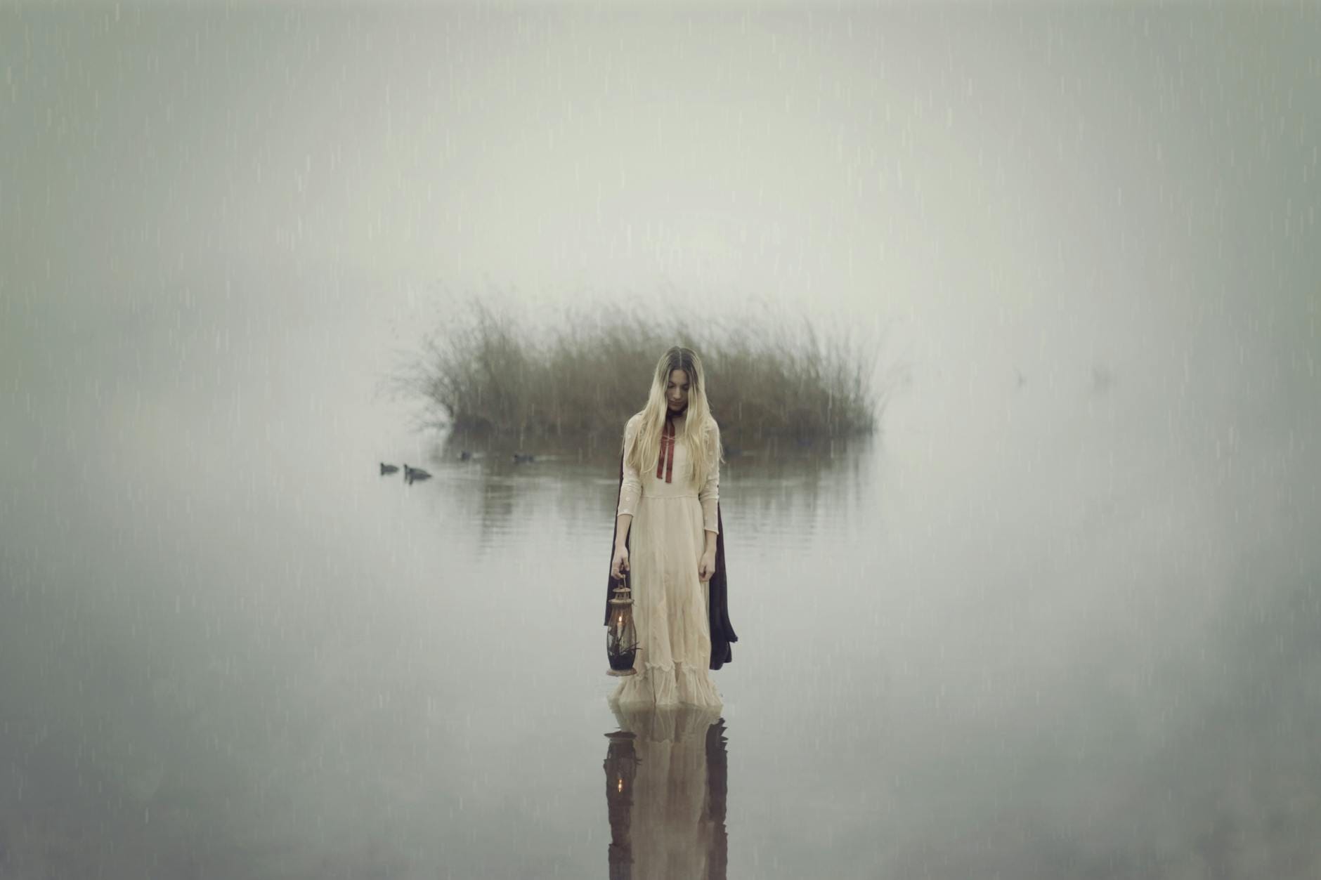 Kobieta w białej sukni z latarnią nad spowitym mgłą jeziorem