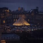 Szklana piramida Luwru nocą, oświetlone muzeum na tle ciemnego nieba
