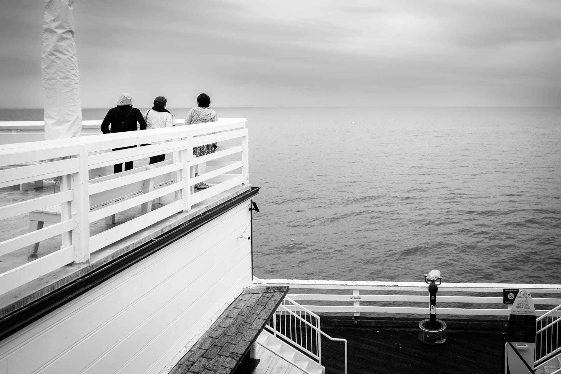 Trzy osoby na molo wpatrzone w morski horyzont w Krynicy Morskiej