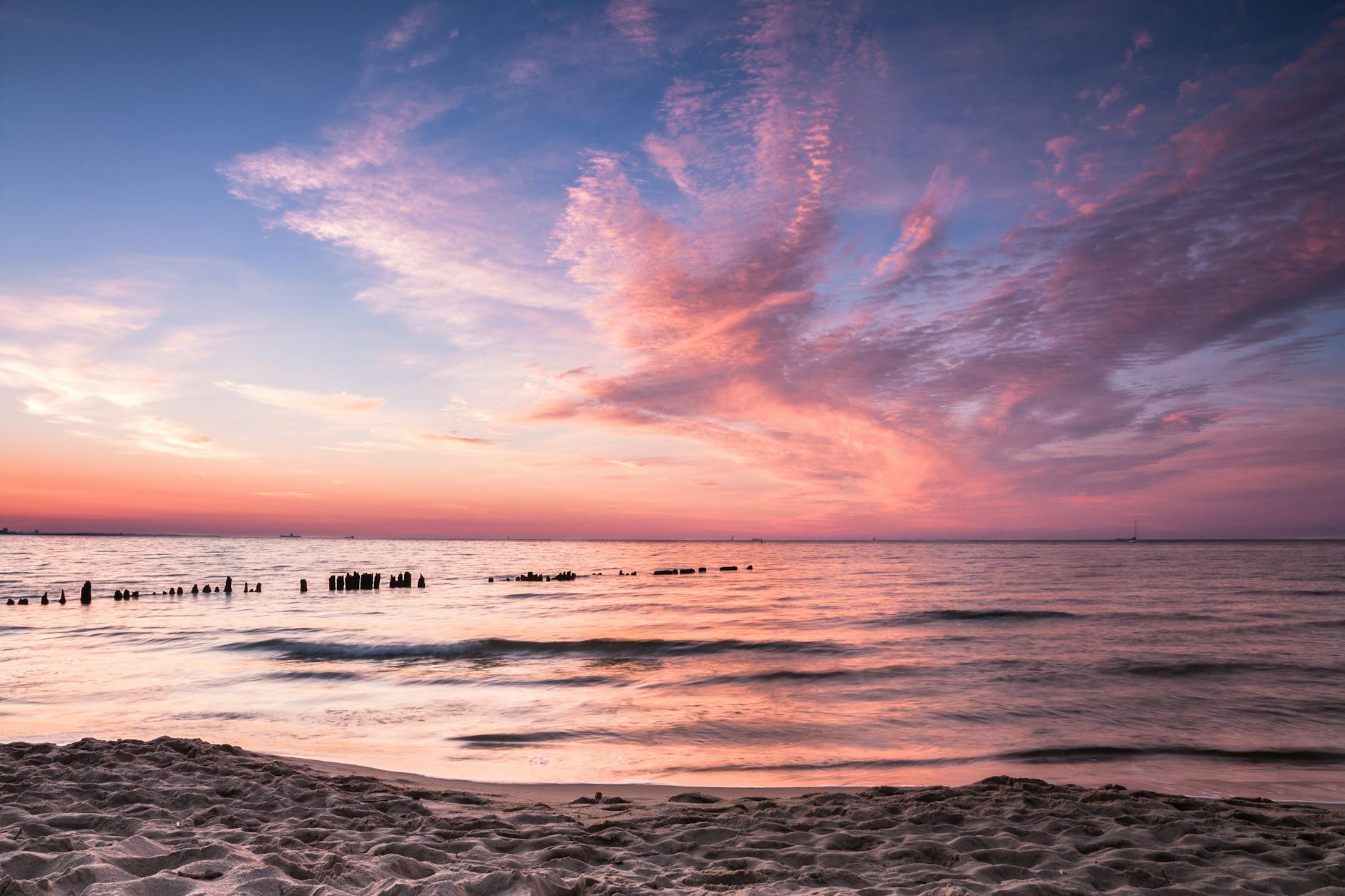 Zachód słońca nad plażą w Gdańsku z różowo-pomarańczowym niebem