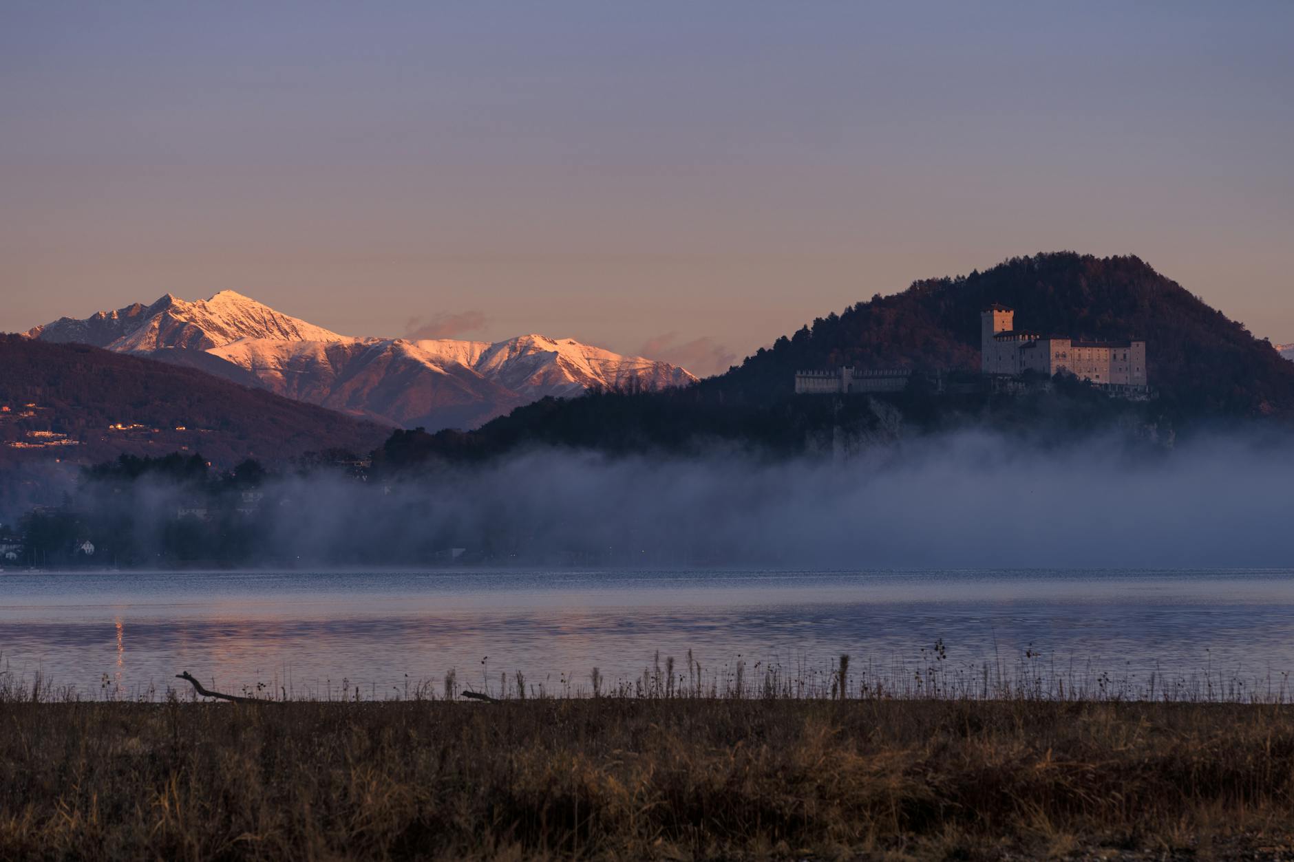 Zamek nad jeziorem Maggiore o świcie, otoczony ośnieżonymi górami