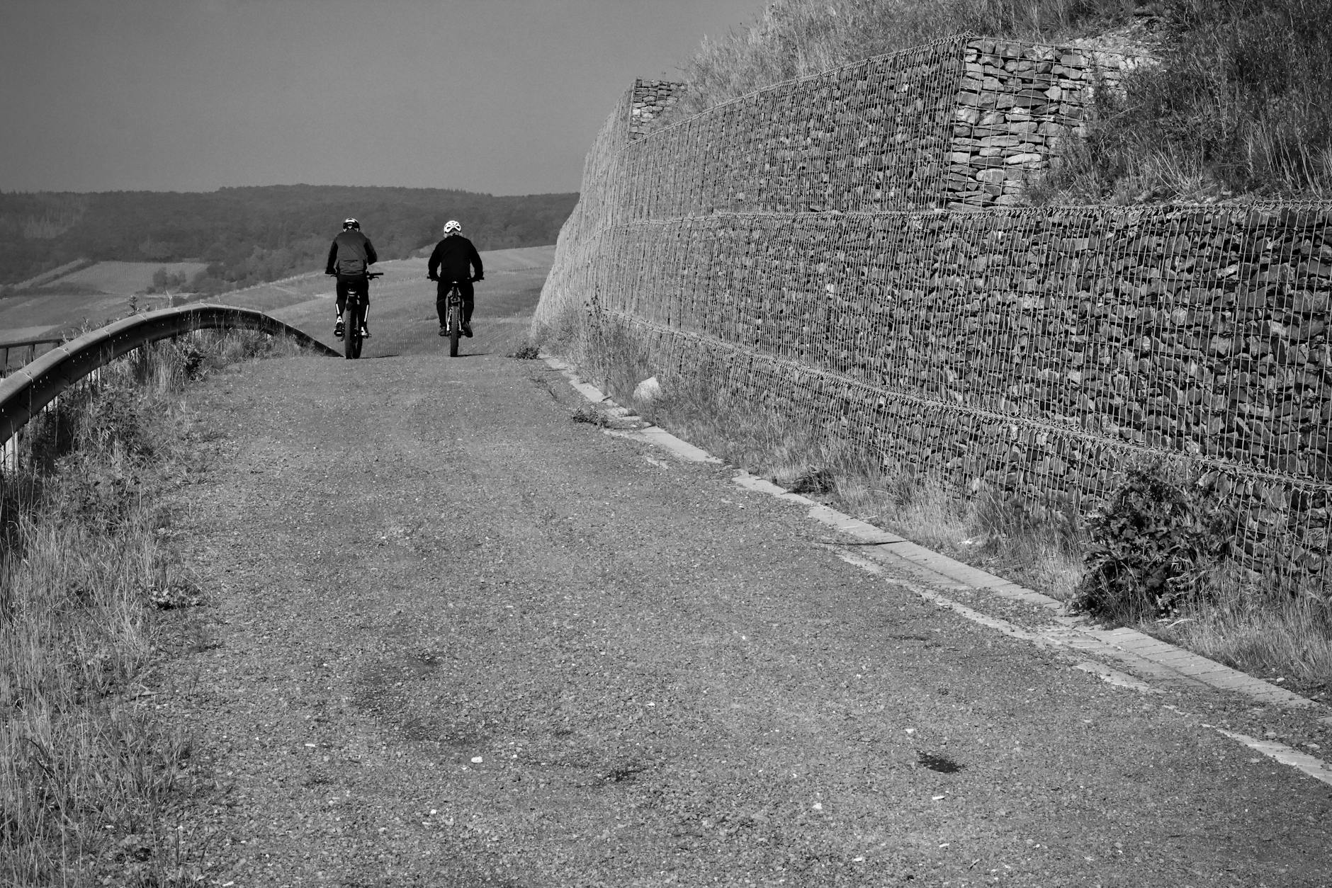 Dwóch rowerzystów jedzie wiejską drogą między kamiennymi murkami